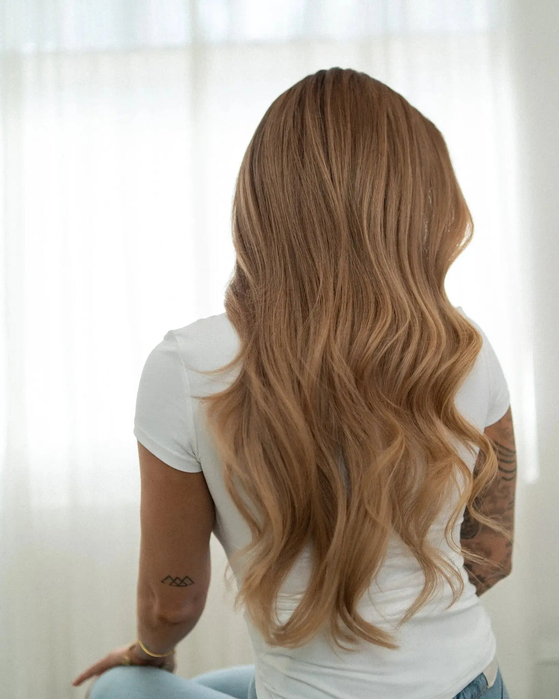 Person with long, wavy hair sitting in a softly lit room.
