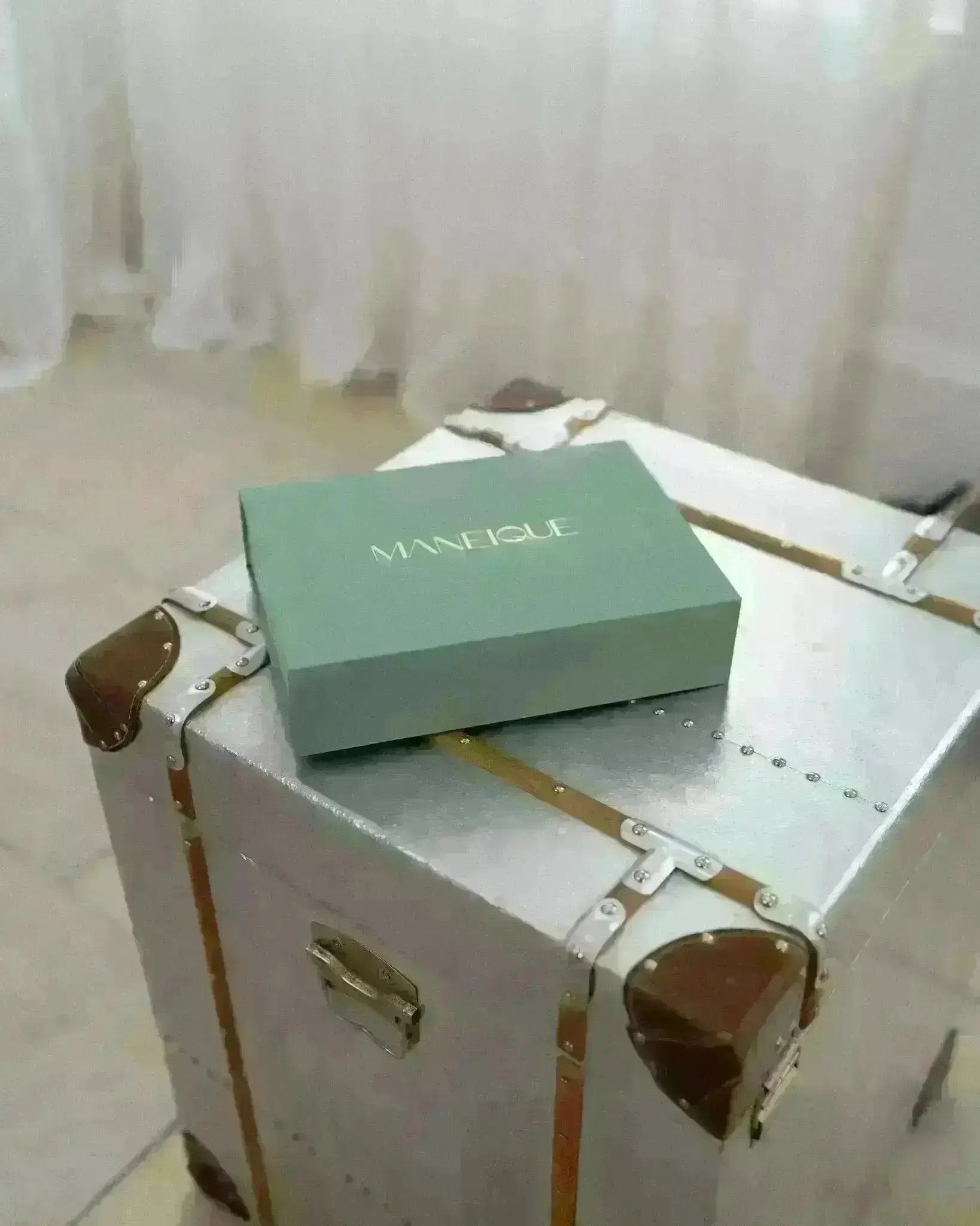 Maneique box on a vintage suitcase with white curtains in the background