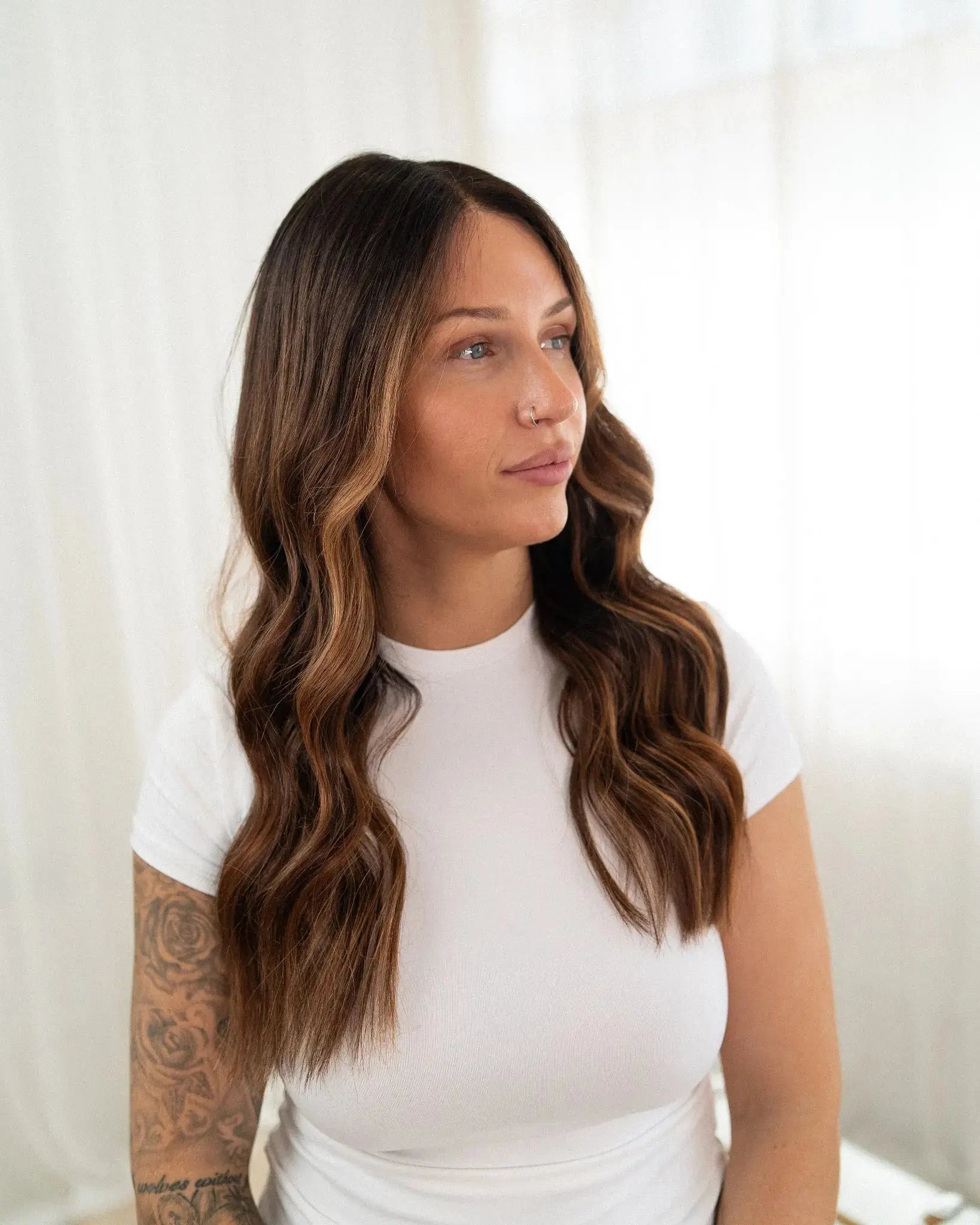 Woman with long, wavy hair wearing a white top against a white background