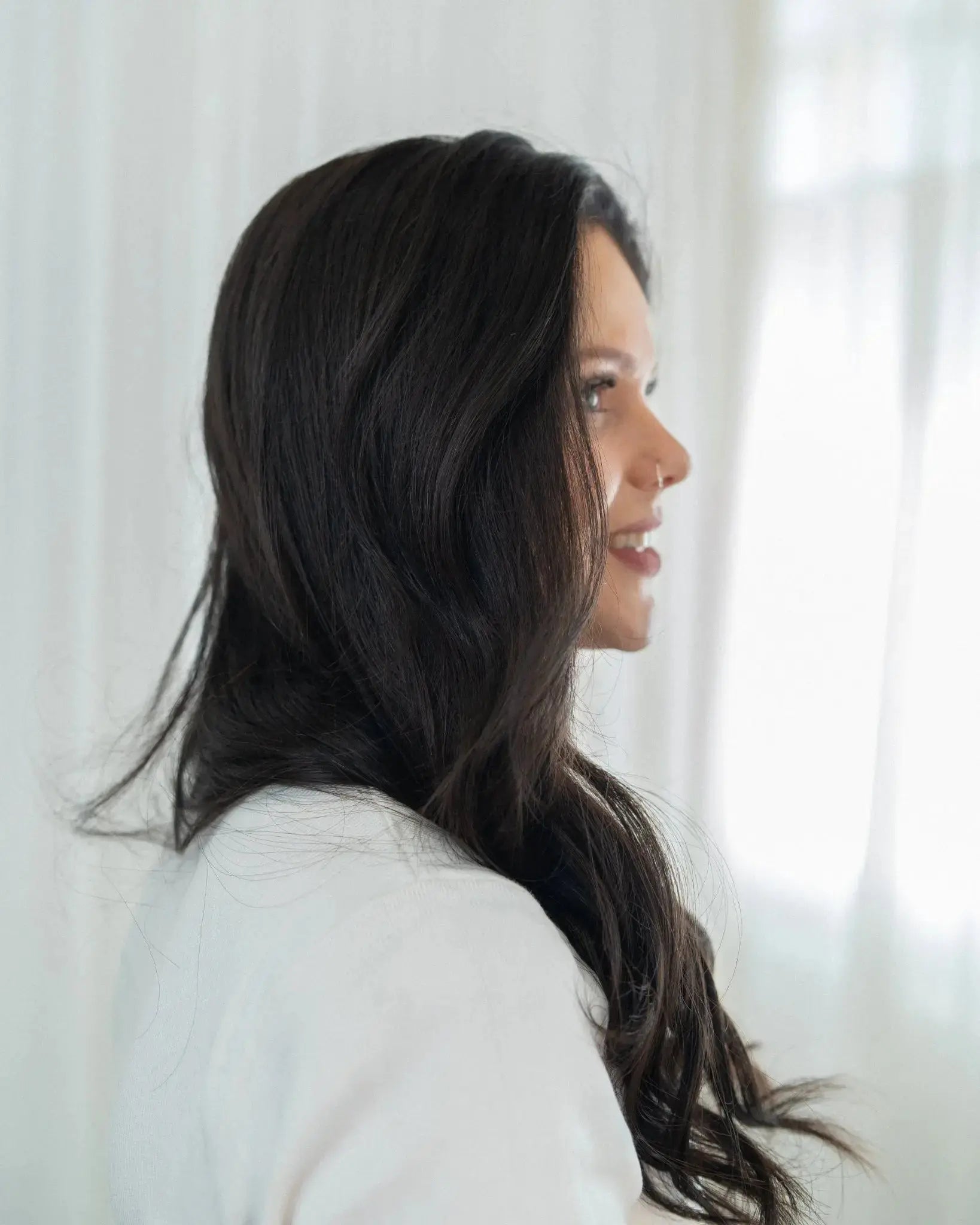 Woman with long dark hair wearing a light gray top against a white background