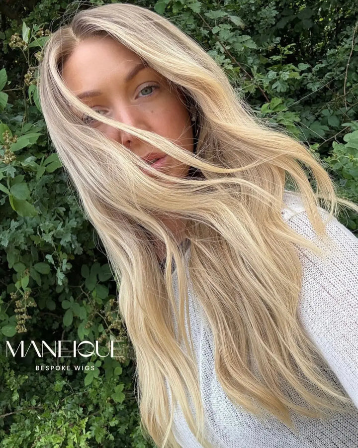 Woman with long blonde wig in front of green foliage, featuring the Maneique logo.